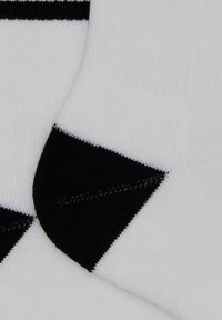 Nahaufnahme von weißen Socken mit schwarzen Zehen- und Fersenbereichen, die eine gerippte Textur und Details der Stricknaht zeigen.