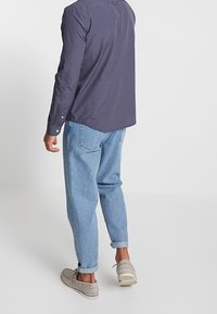 Marineblauw geruit overhemd met lange mouwen gecombineerd met lichtblauwe jeans met een losse pasvorm en beige canvasschoenen. Zichtbare knoopdetails op het overhemd.