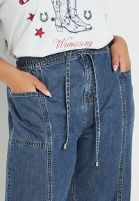 Denim pants with an elastic waistband and drawstring, featuring side pockets and a textured finish in a medium blue color.