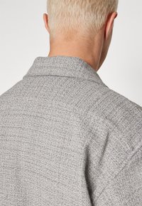 Camicia grigia a trama morbida, con colletto classico e vestibilità rilassata, caratterizzata da un delicato motivo a tessitura sulla superficie.