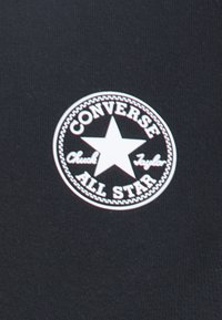 Tessuto nero con un logo bianco circolare di Converse che presenta una stella e il testo "Chuck Taylor" e "ALL STAR" disposto in un motivo circolare.