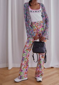 Pantalones de estampado floral colorido en rosa, verde y púrpura, combinados con una camiseta sin mangas blanca. Un bolso negro completa el atuendo.