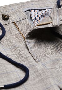 Hellgraue gemusterte Hose mit blauer Karodesign, ausgestattet mit einem marineblauen Kordelzug und einer Reißverschlusstasche mit kontrastierendem gestreiften Stoff innen.