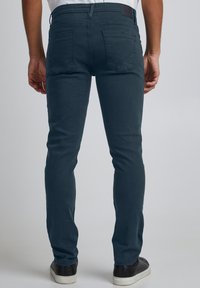 Ozke temno zeleno-modre hlače iz bombažnega blaga z gladko teksturo, z dizajnom s petimi žepi in usnjenim obližem na pasu.