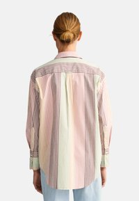 Chemise à rayures multicolores avec des rayures verticales en rose, vert, brun et écru. Manches à boutons et col classique.