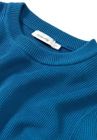 Blå ribbad tröja med rund halsringning, med ett texturerat stickmönster och en etikett med texten "hessnatur" och storlek 36.