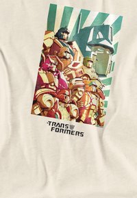 Das Transformers-Grafikdesign auf einem cremefarbenen Shirt zeigt farbenfrohe, stilisierte Roboter mit eckigen Formen und einem kräftigen gestreiften Hintergrund. Darunter steht der Text "TRANSFORMERS."