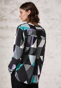 Chemisier à manches longues avec un motif géométrique noir, blanc, sarcelle et lavande ; il présente une coupe décontractée et un col rond, fabriqué en tissu doux.