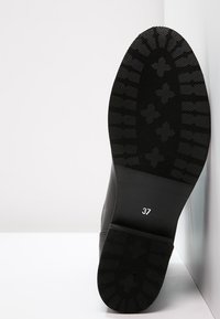 Suela de zapato negra con una superficie de goma texturizada y un patrón de agarre; tamaño marcado como 37. Diseño plano con forma de punta redondeada.
