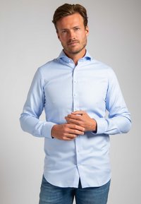 Lichtblauw overhemd van gladde stof met een puntige kraag en lange mouwen, voorzien van een gebogen zoom en knoopsluiting.