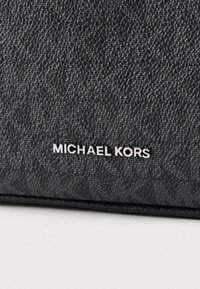 Czarny portfel z teksturowanej skóry z tłoczonym wzorem i srebrnym napisem "MICHAEL KORS" w dolnym prawym rogu.