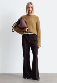 Gemütlicher, übergroßer, brauner Mohair-Pullover, weit geschnittene schwarze Hose, weißer Leder-Gürtel und dunkle Handtasche mit runden Griffen. Strukturiert und lässiger Schnitt.