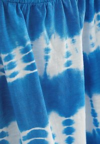 Tissu tie-dye bleu et blanc avec taille élastique froncée, montrant une texture détaillée et des variations de motifs.