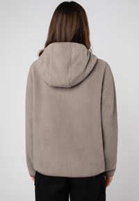 Lichtgrijze fleece hoodie met een zachte textuur, grote capuchon en de onderrand afgewerkt met een contrasterende donkere bies. Vooraanzicht niet zichtbaar.