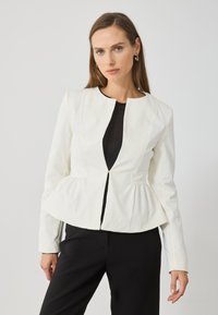 Fehér peplum dzseki kerek nyakkivágással és elülső zipzárral, hosszú ujjakkal és struktúrált fazonnal, fekete nadrággal párosítva.