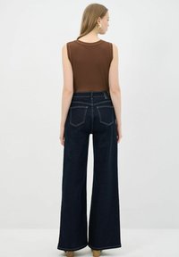 Brązowy bezrękawnik w połączeniu z ciemnoniebieskimi, wysokim talią, szerokimi spodniami dżinsowymi. Charakteryzuje się gładką teksturą oraz kontrastowym szwem na dżinsach.