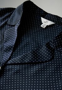 Blusa de color azul marino con lunares blancos, fabricada en una tela suave, con cuello y etiqueta de cuidado visible. La tela drapeada muestra una textura suave.