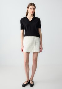 Polo noir à manches courtes associé à une mini-jupe blanche texturée et des ballerines noires à bout rond avec des accents dorés. Design simple et ajusté.