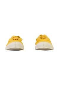 Un par de zapatillas de lona amarillas con suelas y cordones de goma blanca, vistas desde el frente sobre un fondo blanco.