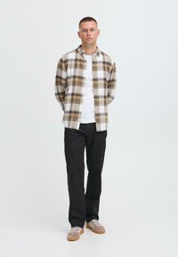Camisa de franela a cuadros en beige y blanco con acentos azules, combinada con pantalones negros y zapatillas beige. Diseño sencillo, estilo de botones.