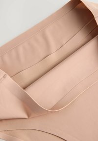 Beige naadloze stoffen kledingstuk met een zachte textuur, voorzien van brede randen en soepele lijnen. Het ontwerp is minimalistisch en onverfraaid.
