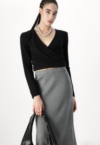 Top negro de manga larga y envolvente, falda midi acanalada gris y un bolso negro. El conjunto presenta un escote en V profundo y una silueta ajustada.