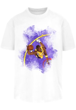 Hvit T-skjorte med et lilla akvarellsprutdesign, med en basketballspiller i en gul drakt, en oransje basketball og røde kurvdetaljer.