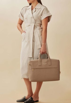 Malette en cuir beige avec une surface texturée, des poignées supérieures doubles et une poche zippée à l'avant. Modèle portant une robe en lin légère.