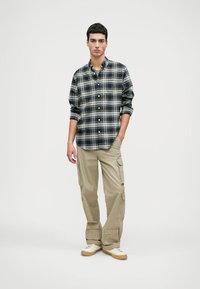 Rutet flanellskjorte i marineblått, grønt og hvitt, med knappede mansjetter. Beige cargo-bukser med sidelommer. Uformelle joggesko i hvitt og beige.