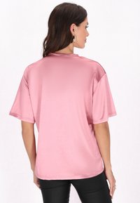 Rosa satinvare oversized t-shirt med korte ærmer, rund halsudskæring og glat tekstur, set fra ryggen.