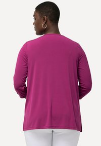 Maglietta a maniche lunghe di un vivace magenta, con collo rotondo e vestibilità ampia. Texture liscia con spacchi laterali per facilità di movimento.