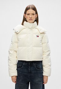 Krótka, puchowa kurtka w kolorze off-white, wykonana z błyszczącego materiału. Posiada wysoki kołnierz, zapięcia na napy oraz haftowane logo na klatce piersiowej.