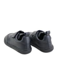 Zapatos sintéticos negros con acabado suave, punta redondeada y correa de Velcro. Presentan una suela de goma texturizada y una lengüeta en la parte posterior para facilitar su uso.