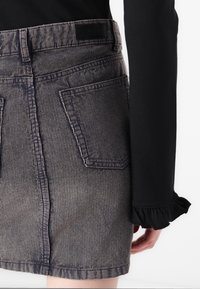 Fustă mini din denim cu un model de dungi verticale, având talie înaltă, două buzunare pe spate și un finisaj texturat. Țesătura neagră apare de sub manșetă.