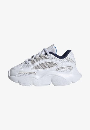 Biały sportowy sneaker z teksturowaną podeszwą, siateczkową i syntetyczną cholewką, białymi sznurówkami oraz ciemnoniebieską wyściółką, widziany z boku.