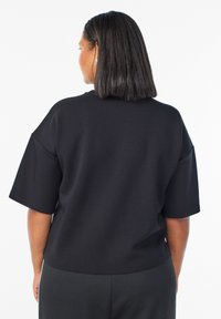 Juodas per didelis marškinėliai iš lygaus, medvilninio audinio, su trumpomis rankovėmis. Paprastas, nepuošnus dizainas su apvaliu iškirpimu ir laisvu siluetu.