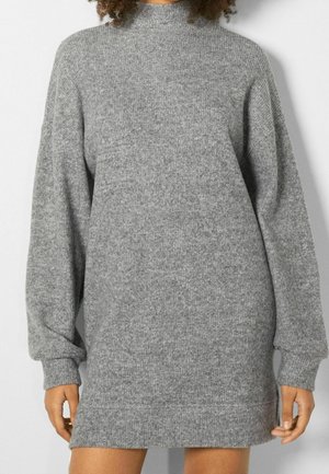 Graues Strickkleid mit hohem Kragen, langen Ärmeln, gerippter Textur und lockerer Passform, das oberhalb der Knie endet und seitliche Schlitze hat.