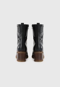 Bottines en cuir noir avec une texture lisse, fermeture éclair à l'arrière et talons en bois massif. Design simple et discret.