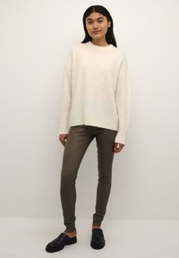 Kremowy, oversize'owy sweter wykonany z miękkiego materiału, w połączeniu z dopasowanymi oliwkowymi spodniami i czarnymi klapkami. Minimalistyczny design, bez wzorów.