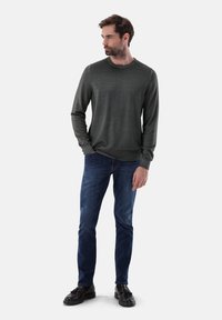 Grauer Strickpullover mit Rundhalsausschnitt, langen Ärmeln und gerippten Bündchen, kombiniert mit blauen Jeans und schwarzen Lederschuhen.