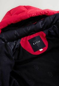 Chaqueta roja y negra con capucha; presenta un forro de forro polar, etiqueta de tela y un sutil logotipo en el interior. Textura suave en toda la prenda.