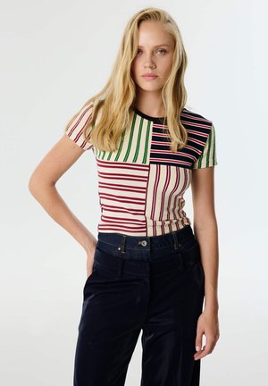 T-shirt a righe con un design a blocchi di colore, con strisce rosse, verdi e blu navy su uno sfondo crema, maniche corte e scollo rotondo.