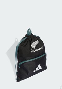 Mochila negra con cordón y detalles en azul verdoso, que cuenta con un bolsillo frontal con cremallera, el logo "ALL BLACKS" y la marca Adidas. Material texturizado.
