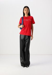 Red cotton T-shirt with white "TOMMY HILFIGER" logo, paired with black faux leather wide-leg pants, and a blue shoulder bag.