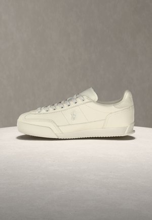 Witte leren lage sneaker met vetersluiting, gestructureerd zijpaneel en subtiel reliëflogo op een lichte grijze ondergrond en achtergrond.