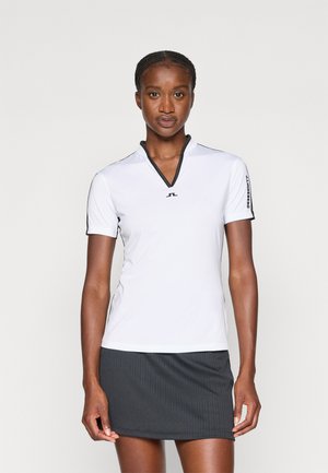 Biela krátk 色o rízna košeľa s výstrihom do V, s čiernymi akcentami pozdĺž výstrihu a rukávov. Hladká, ľahká látka.