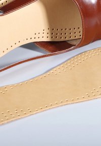 Brown leather sandal featuring a smooth upper and perforated beige insole, highlighting detailed stitching and texture.