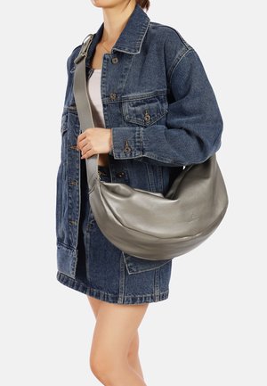 Borsa hobo grigia in pelle con una texture liscia e una forma curvata, portata a spalla, abbinata a una giacca e una gonna di denim.