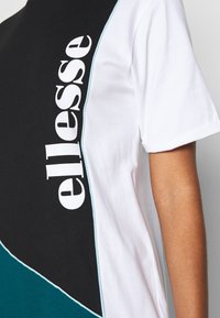 T-shirt à blocs de couleurs avec sections noire, blanche et turquoise. Logo "ellesse" bien visible en blanc, matière coton douce, coupe décontractée.