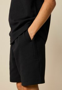 Pantalones cortos de algodón negros con un corte holgado, que cuentan con bolsillos laterales, una textura suave y un diseño sencillo, cortados hasta la altura de la rodilla.